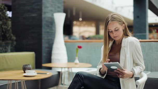 Woman works with a tablet sitting at the table in the cafe — Stock Video