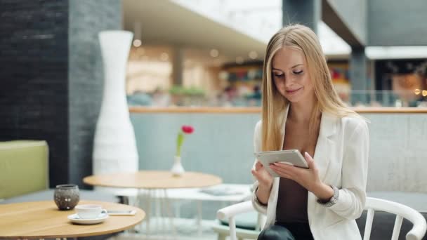Жінка працює з планшетом, що сидить за столом у кафе — стокове відео