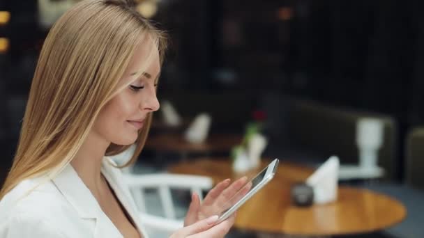 Γυναίκα λειτουργεί με ένα tablet που κάθεται στο τραπέζι στην καφετέρια — Αρχείο Βίντεο
