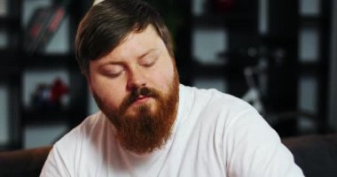 Sakallı şişman adam ayı içecekler ve Mısır ile masadan elinde uzaktan kumanda ile Tv izliyor