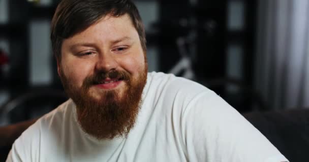 Sourire gros homme avec barbe regarde la télévision dans la chambre — Video