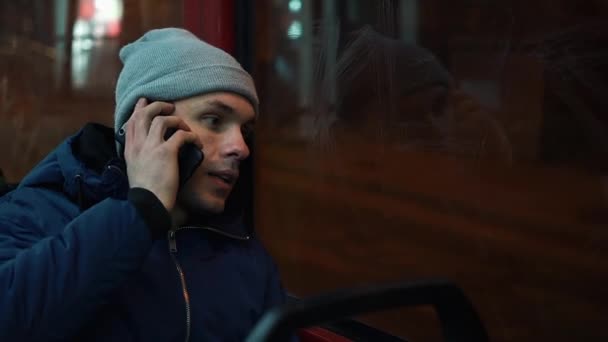 Lonely young man rides in a tram and talks on the phone in the night — Stock Video