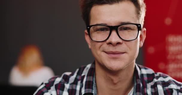 Mosolygó fiatal férfi a szemüveg néz ki, egyenesen a kamera — Stock videók