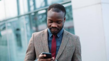 Yorgun Afrikalı-Amerikalı işadamı bir şey ayakta dışında onun smartphone içinde okur. Adam sms manifatura app City akıllı telefon kullanma