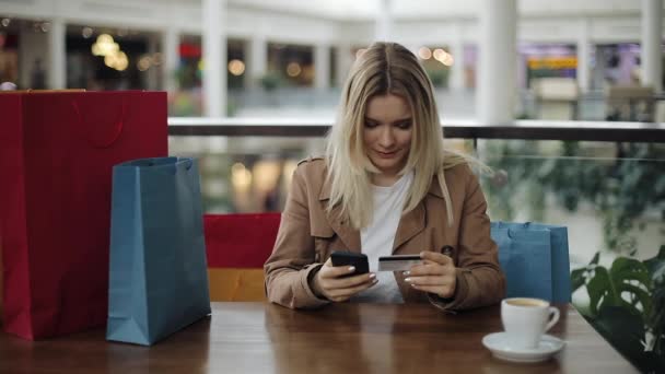 Flicka wirtes ett antal kreditkort som sitter med shoppingkassar i caféet — Stockvideo