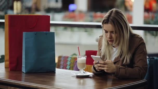 Chica llama a un número en el teléfono sentado en el café con bolsas de compras en la mesa — Vídeos de Stock