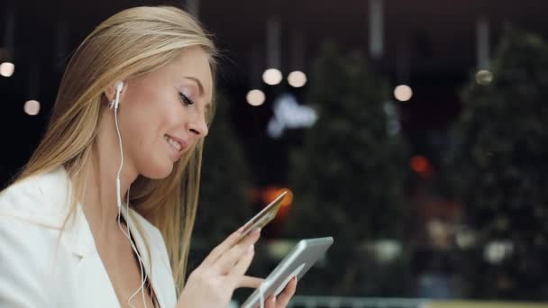 Una giovane donna sorridente prende un dato dalla carta di credito dorata che lavora con un tablet — Video Stock