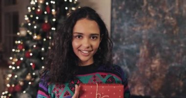 Güzel Mutlu Kadın 'ın portresi Ellerinde Güzel Hediye Kutusu Tutuyor ve Noel Ağacı' na yakın rahat bir arka planda duran kameraya gösteriyor. Noel ve Yeni Yıl Kutlama Kavramı.