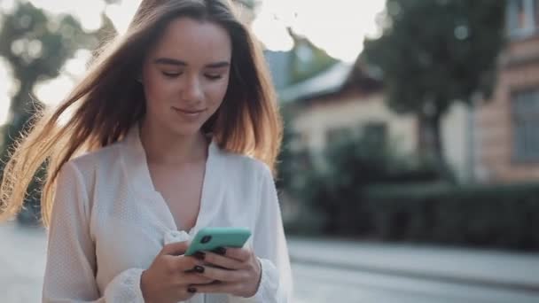 Close Up na mladé krásné bruneta dívka pomocí svého moderního mobilního telefonu a rozhlížet se kolem při chůzi na útulné ulici. Koncepce technologie a komunikace. — Stock video