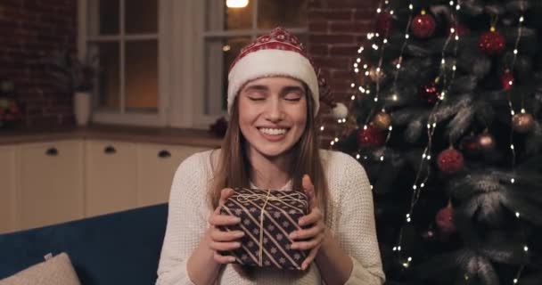 活気に満ちた社交的な笑顔魅力的な若い女性はクリスマスホーム背景に座っています。女の子がコンピュータ画面のウェブカメラビューを見てキスを吹いてプレゼントを与えるチャットを振る. — ストック動画