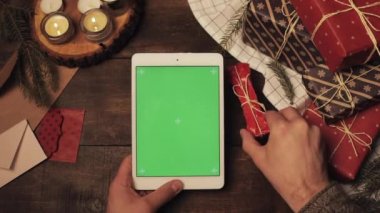 Top View of Hands Srapped Present Bone, Hediye Kutularının Düzeltilmesi ve Beyaz Yeşil Ekran Tabletinin Üzerinde Mumlarla süslenmiş Noel Masası Tutulması. Model.