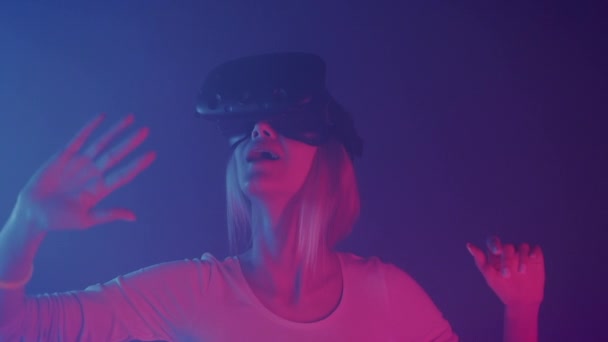 Close Up of Happy Young Girl in Virtual Reality Headset Play Game and Moving Hands in Air Standing in the Room with Neon Lighting Colors Futurictic Background (англійською). Vr Concept. — стокове відео