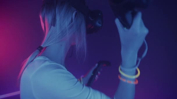 Rückansicht eines Mädchens mit Virtual-Reality-Brille, das Steuerknüppel beim Spielen hält und die Hände vor Neonbeleuchtung bewegt. vr, Unterhaltungskonzept. — Stockvideo