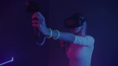 Young Girl Wearing Virtual Reality Headset Holding Joystick or Controllers, Doing Archery. Woman Playing Game at the Abstract Neon Lighting Background. VR, Entertainment Concept.