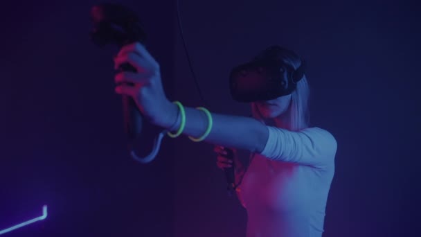 Junges Mädchen mit Virtual-Reality-Headset, das Steuerknüppel oder Controller hält und Bogenschießen macht. Frau beim Spiel auf dem abstrakten Neonlicht-Hintergrund. vr, Unterhaltungskonzept. — Stockvideo