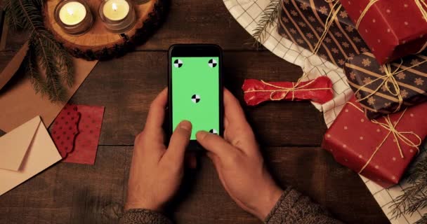 Vista superior das mãos tocando na tela verde vertical do novo smartphone na mesa decorada de madeira de Natal. Chroma Key. Conceito de Natal férias . — Vídeo de Stock