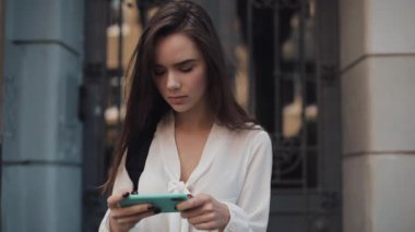 Omzunda çantasıyla ve Smartphone 'uyla Eski Bina Arkaplanında Yürüyen Yatay Peyzaj Modu ile Güzel Esmer Kız.