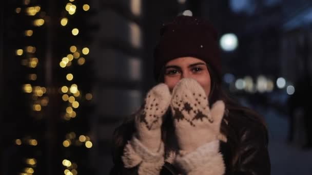 Junge schöne kaukasische Mädchen tragen Winterkleidung, lächeln, schauen in die Kamera, posieren zu Fuß an Weihnachten dekorierten Abend Straße background.holiday Konzept. — Stockvideo
