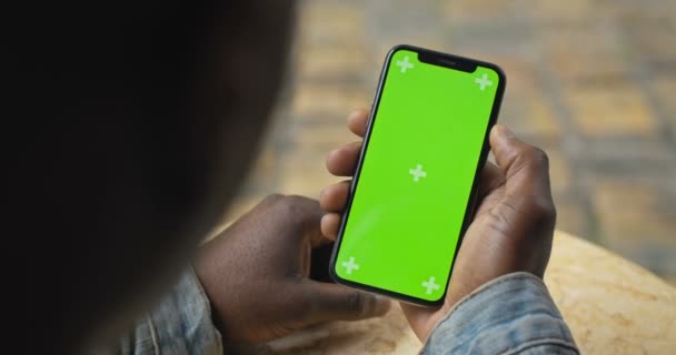 Gros plan Vue de la tête et de la main d'un Afro-Américain tenant son Smartphone avec écran vert et le regardant, défilant, écran tactile. Vue de derrière. Maquette . — Video