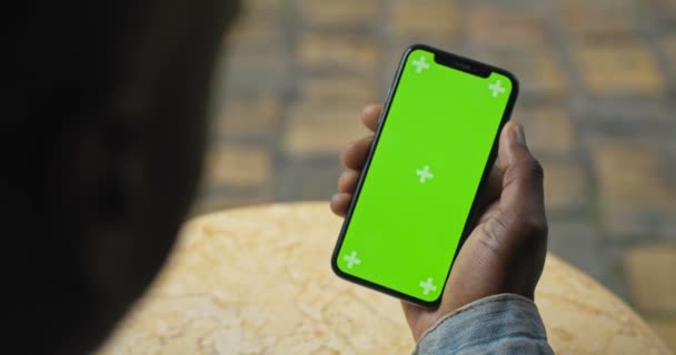 Gros plan Vue de la tête et de la main d'un Afro-Américain tenant son Smartphone avec écran vert et le regardant et l'écran tactile. Vue de derrière. Maquette .