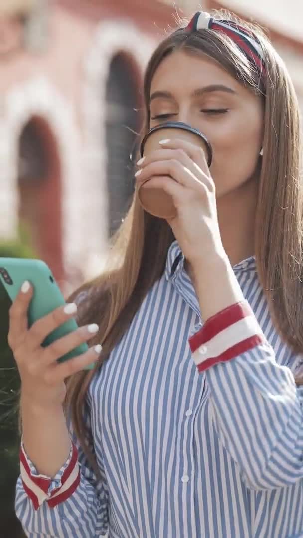 Pionowe wideo. Close Up of Young Charming kaukaska kobieta z opaską na głowie w stylowej koszuli w paski przy użyciu jej smartfona przewijanie i uśmiech patrząc szczęśliwy picia kawy — Wideo stockowe