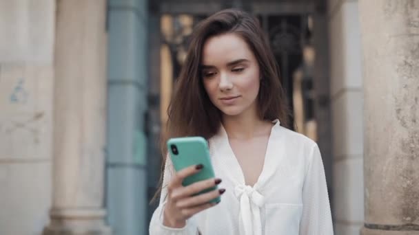 Pretty Mladá bruneta dívka kráčí na útulné Old Town Architecture Backgroud při použití svého telefonu, říkat Wow a usmívání. Koncepce komunikace a techniky. — Stock video