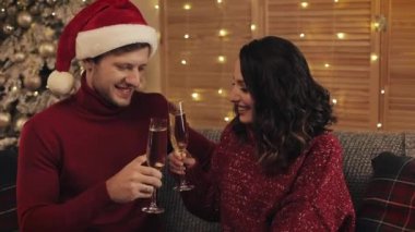 Lovely Young Couple Sitting on the Sofa near Christmas Tree at Cosy Home Background Kissing and Raising Glasses of Champagne Concept of Holidays and New Year. Close Up.