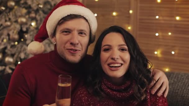 Portret van Cheerful Young Caucasian Couple zittend op de bank bij de kerstboom. Familie zwaaien videogesprek glimlachen op zoek naar de camera en zeggen groet concept van huwelijksvakanties en Nieuwjaar. — Stockvideo