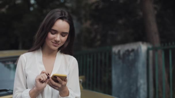 Gros plan de jeune belle fille brune utilisant son smartphone moderne pour la communication, Dactylographier un message tout en se tenant debout à l'extérieur avec Vintage Golden Car à l'arrière-plan . — Video