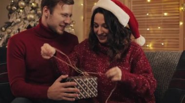 Sevgili genç çift Noel hediyesi bandajlama bantlarını birleştiriyor ve Ev Arkaplanı 'ndaki Noel Ağacı' nın yanındaki koltukta oturan fiyonkla bağlanıyor. Tatil ve Yeni Yıl kavramı.