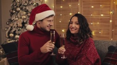 Hoş bir çift Noel ağacının yanındaki koltukta oturuyor. Evin arka planında, kameraya bakan şampanya kadehlerini tokuşturuyor. Tatil ve Yeni Yıl Kapanışı kavramı.