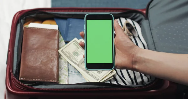Νεαρή γυναίκα ετοιμάζεται για ταξίδι. Κρατάει smartphone με πράσινη οθόνη στο φόντο της βαλίτσας. Κλειδί χρωμίου. — Φωτογραφία Αρχείου