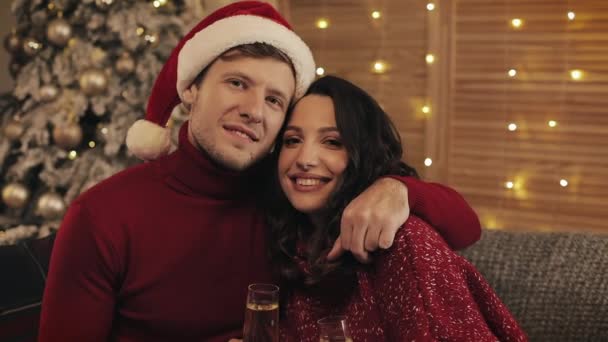Porträt eines hübschen jungen Paares, das auf dem Sofa in der Nähe des Weihnachtsbaums vor heimeligem Hintergrund sitzt und Sektgläser klimpert. Familie blickt auf Kamerakonzept für Urlaub und Neujahr aus nächster Nähe.