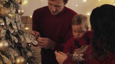 Mutlu Gülümseyen Bebek 'in ailesi, Parlak, rahat oturma odalarında Noel Ağacı süslüyor. Kadınlar Bebeği Ellerinde Tutar Oyuncak Kar Tanesi Verir ve Sarılır.