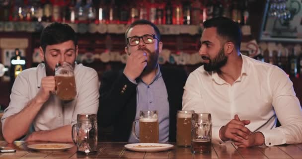 Tři staří přátelé popíjejí točené pivo a mluví ve sportovním baru. Fotbaloví fanoušci se smějí a diskutují o novinkách v pivnici. — Stock video