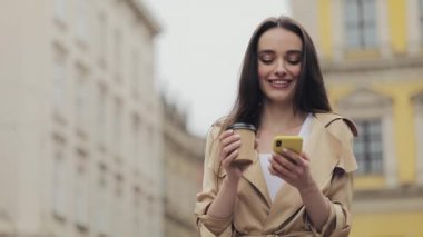 Çekici Genç Kız Akıllı Telefonunu Kullanıyor ve Elinde Kâğıt Kupa Tutarak Gülümsüyor İçiyor Kahve İçiyor Eski Şehir Arkaplan Görünümü 'nde Duruyor.