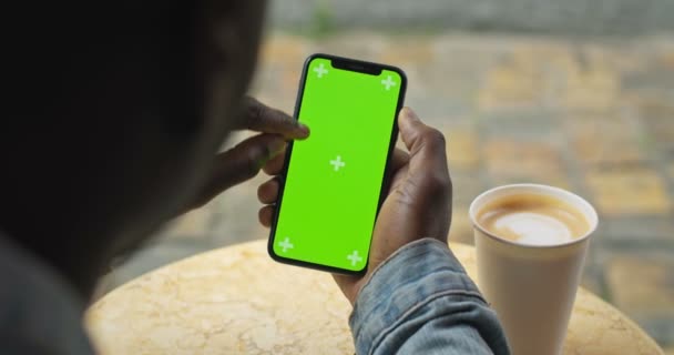 Lviv, Ukraine - Le 09 août 2019 : Des mains d'Afro-Américain assis à table avec une tasse de café en papier tenant un smartphone avec écran vert, le regardant, défilant, écran tactile . — Video