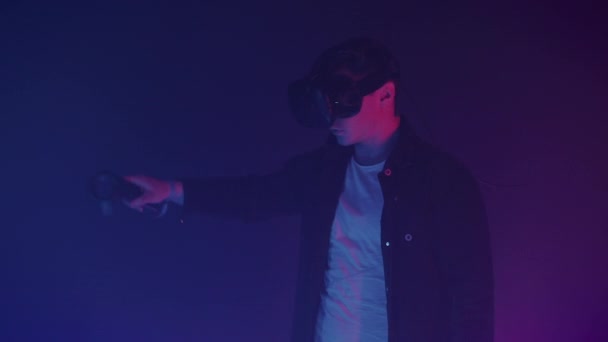 Attraktive Man in Virtual Reality Glasses tegner abstrakte linjer og figurer ved hjelp av Controllers, som står i rommet med neonlys Futuritisk bakgrunn . – stockvideo