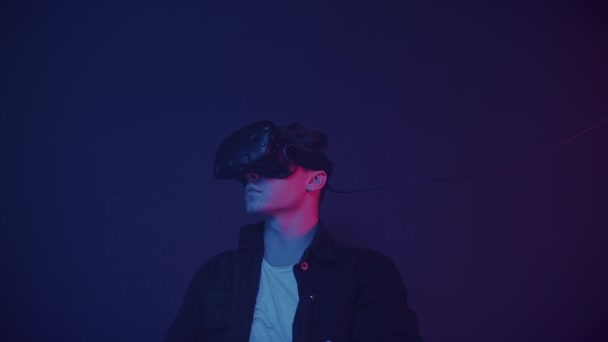 Detailní záběr mladého muže s brýlemi virtuální reality, pohyblivé ruce, práce s virtuální obrazovkou, stojící v místnosti s abstraktní neonové osvětlení barvy pozadí. Koncept budoucnosti. — Stock video