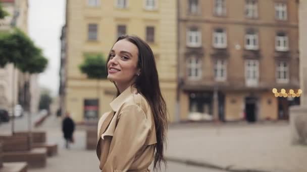 Backside Tracking bilder av attraktiva unga flicka promenader othe gator ser tillbaka över hennes axel och vänder sig om leende för kameran. — Stockvideo