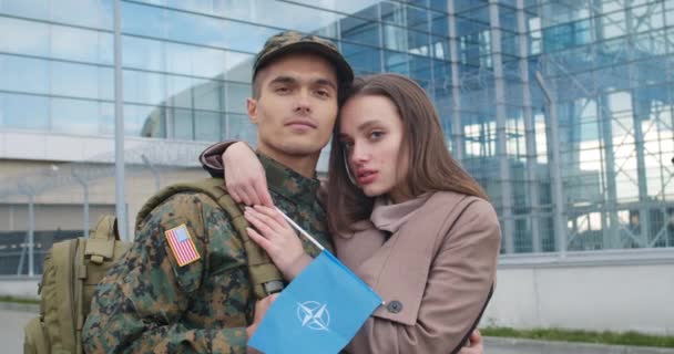 Lviv, Ukraine - October 30, 2019: Portrait of couple with NATO flag looking to camera. Close up of young girl and her military boyfriend standing near airport. People portraits. — 비디오