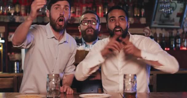 Tres viejos amigos felices bebiendo cerveza y viendo el partido de fútbol en el pub. Animan y celebran la victoria de su equipo . — Vídeo de stock