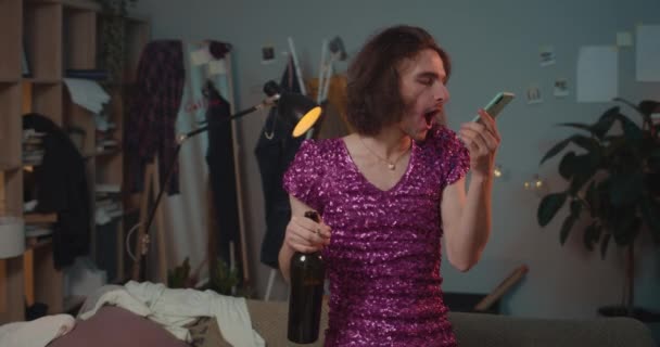 Front view of man transgender standing with wine bottle and yelling at boyfriend . Drunky transvestite man in dress with sequins holding smartphone and screaming at friend. — Stock Video