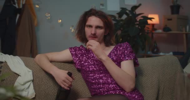 Zbliżenie nieszczęśliwego pijanego transseksualisty siedzącego na kanapie jedzącego czekoladę i patrzącego w kamerę. Mężczyzna trans czuje się samotny i smutny trzymając butelkę wina. Pojęcie ludzi i emocji. Dobry wieczór.. — Wideo stockowe