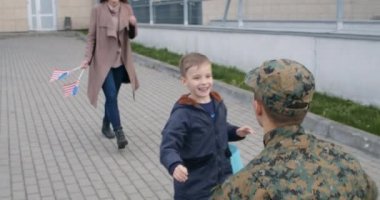 Dışarıda askerlerle tanışan güzel bir eş ve oğul. Küçük mutlu çocuk evine hoş geldin posteri atıyor ve askerî babasına koşuyor. Asker ailesi kucaklaşıyor. Birleşme kavramı.