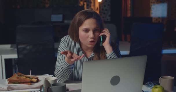Dissapointed female office worker talking on phone with her boss , telling her to finish lot of work for tomorrow. Woman using laptop and having phone conversation at night office. — 비디오