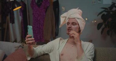 Kanepede oturmuş telefonda video sohbeti yaparken, el kol hareketi yaparken ve gülerken transseksüellere yakın dur. Kafasında havlu olan genç bir transseksüel akıllı telefon kullanıyor, çikolata yiyor ve parmaklarını yalıyor..
