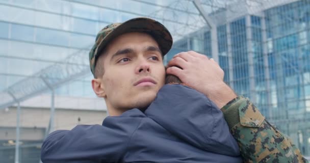 Detailní záběr mladého vojáka objímajícího syna před odchodem do armády. Dítě v náručí vojenských otců. Vojenská služba a služba. Pojem rodinného vztahu rodičovská láska. Venku. — Stock video