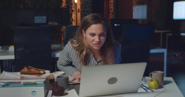 Boze zakenvrouw schreeuwend en verkruimelend papier tijdens het werken op laptop. Gestresst meisje vinden fout en kijken geïrriteerd terwijl zitten aan het bureau in lege nacht kantoor . — Stockvideo