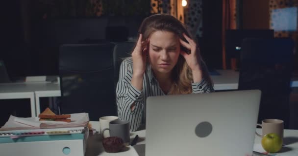 Framifrån av trött affärskvinna massera mallar och panna för att koncentrera sig medan du arbetar långa timmar Utmattad flicka med hjälp av sin dator på tom natt kontor. Begreppet överarbete. — Stockvideo